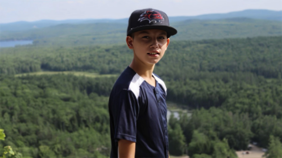 Boy wearing blue shirt and hat with mountains in the background