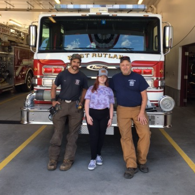 novalee stands in front of a firetruck with two firefighters