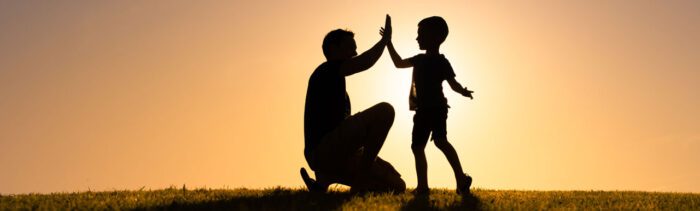 Father and sun high fiving outside with the sun setting in the background.