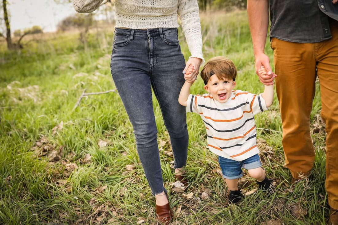 Otto holding his mom and dads hands walking in the grass.