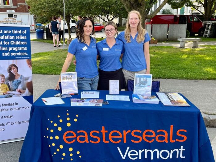 Krist, Devyn, and Tayna posing for a picture standing behind an Easterseals VT table outside.