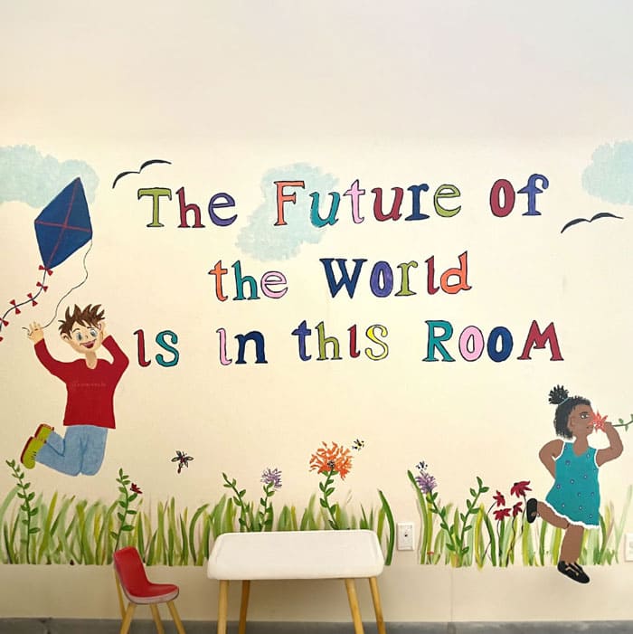 Wall drawing of boy flying a kite and little girl running. Wall text reads, "The future of the world is in this room."