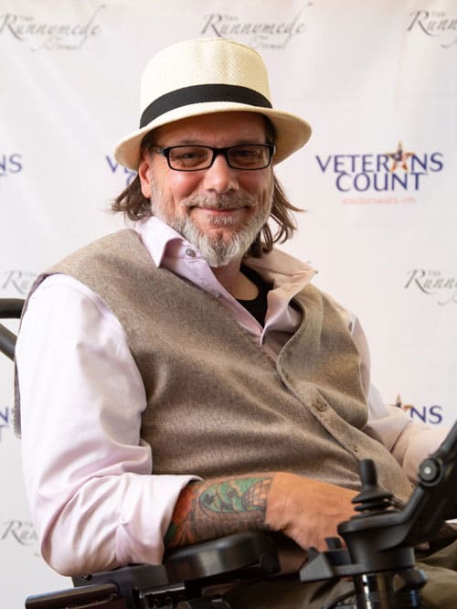 Photo of Mike sitting in his wheelchair smiling for a photo in front of an Easterseals Veterans Count backdrop.